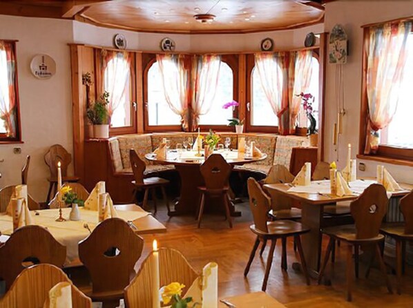 A dining area with wooden tables and chairs, a central round table, and large windows with curtains. - Kräuter Chalet (Furtwangen)
