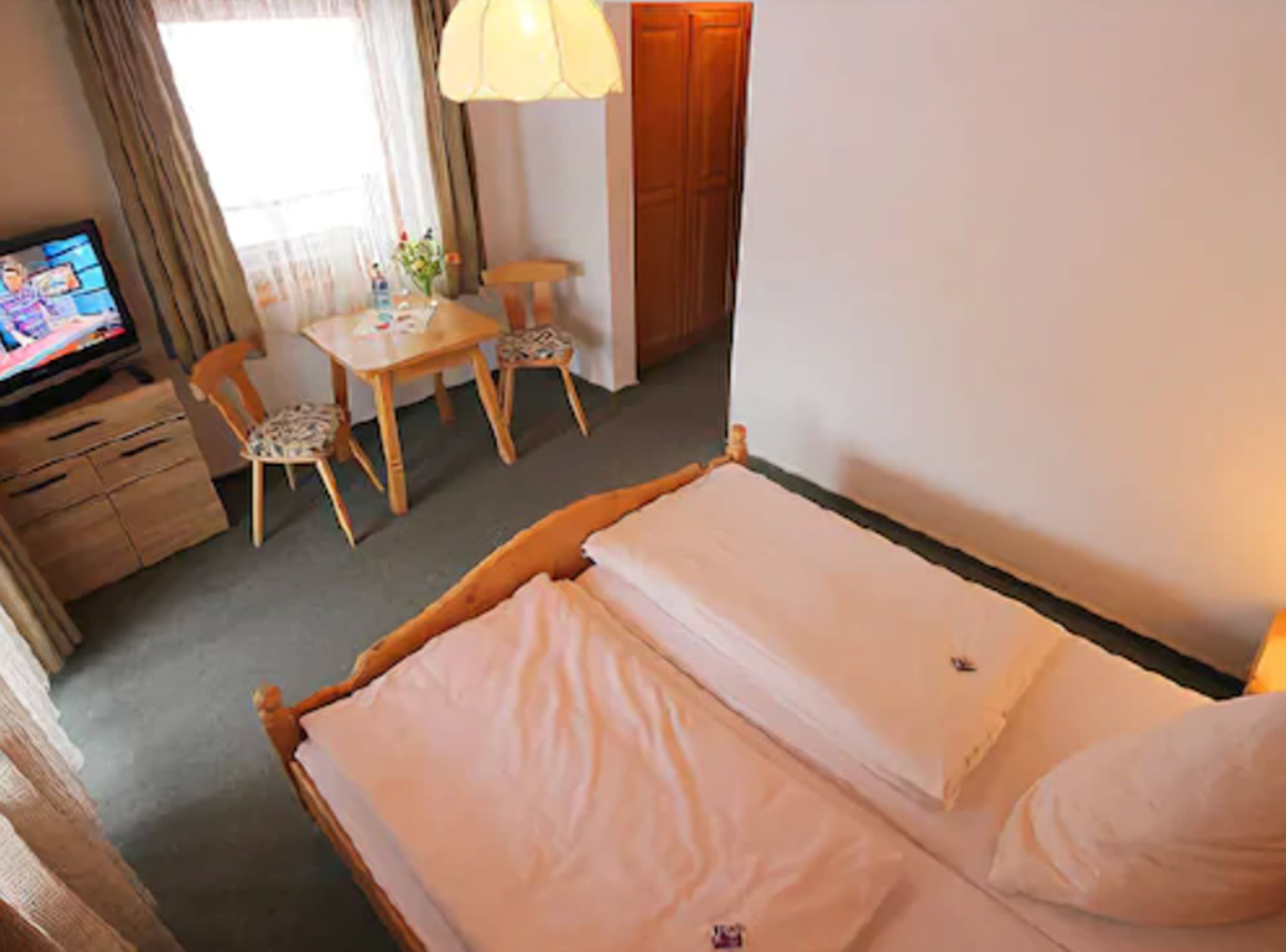 Habitación de hotel con cama, escritorio, dos sillas, televisor y ventana con cortinas.