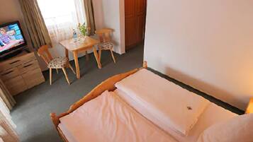 Habitación de hotel con cama, escritorio, dos sillas, televisor y ventana con cortinas.