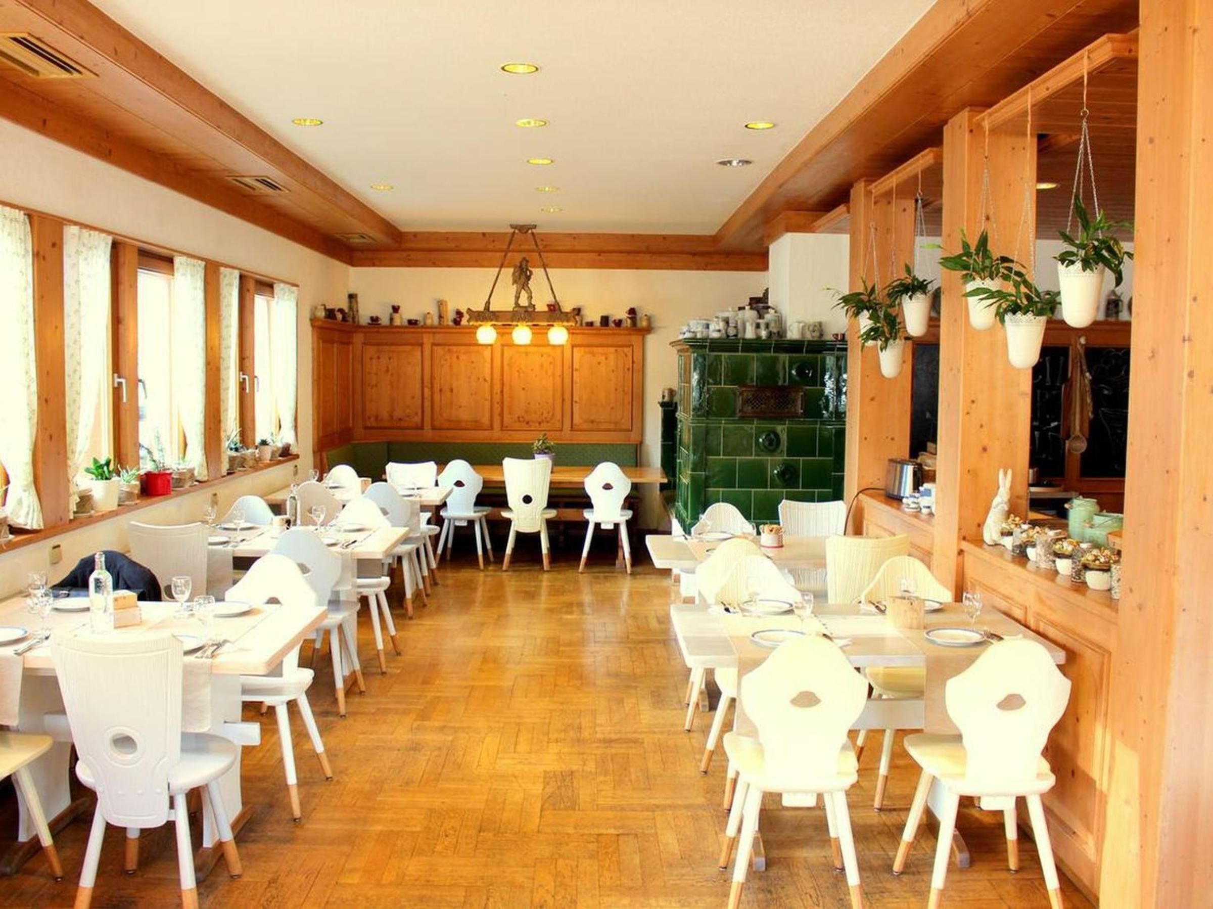 Un vaste espace dédié à la salle à manger, avec des murs en bois et un poêle vert, agrémenté de chaises et de tables blanches.