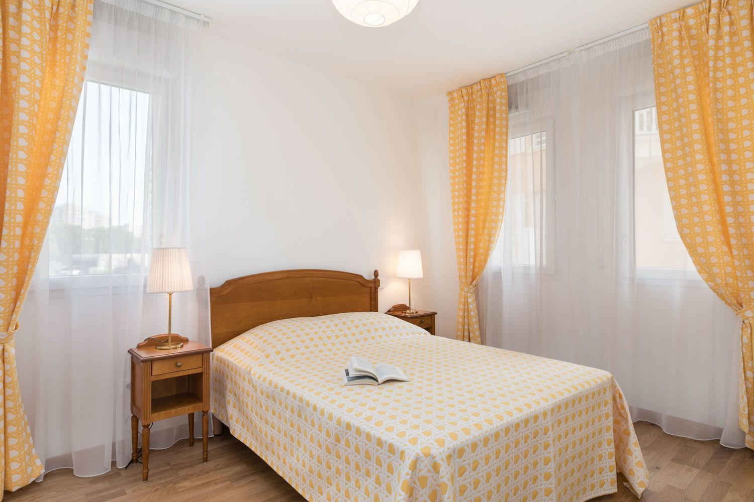 A bedroom with a wooden bed, two bedside tables with lamps, and yellow patterned curtains.