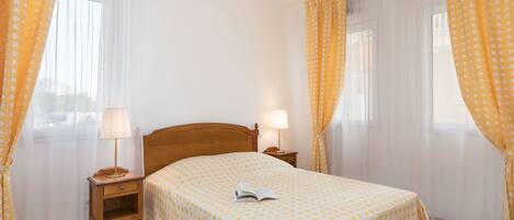 A bedroom with a wooden bed, two bedside tables with lamps, and yellow patterned curtains.