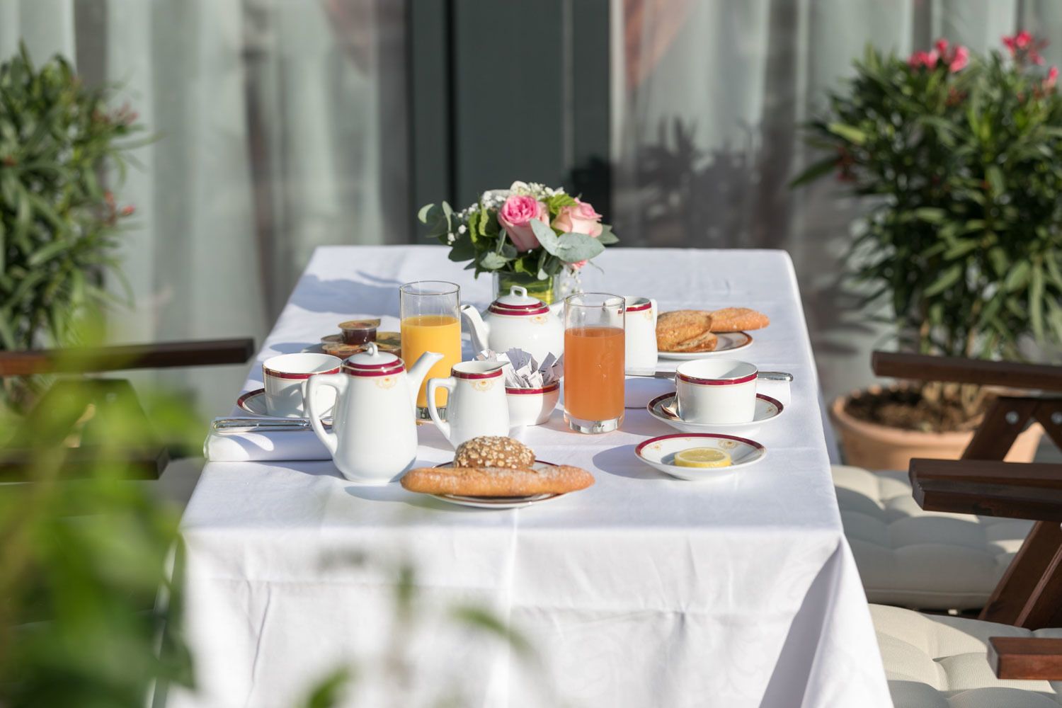 A table set for breakfast with coffee, tea, juice, and pastries, surrounded by potted plants.
