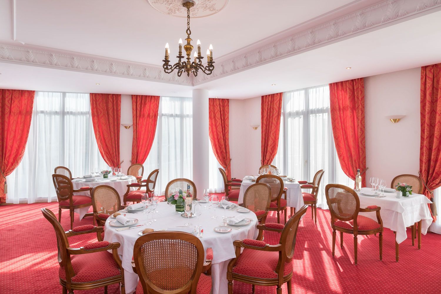 A dining room with round tables, red curtains, and chandeliers.