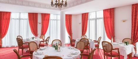 A dining room with round tables, red curtains, and chandeliers.