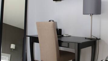 Habitación de hotel con escritorio, silla, televisor de pantalla plana, lámpara y un espejo grande.