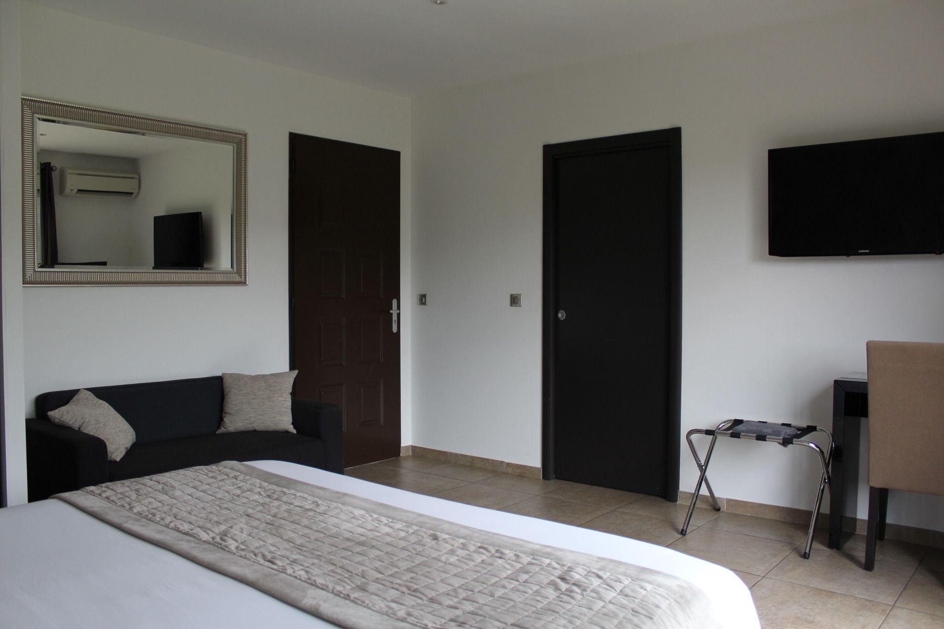 A bedroom with a bed, a sofa, a TV, a door, and a small table.