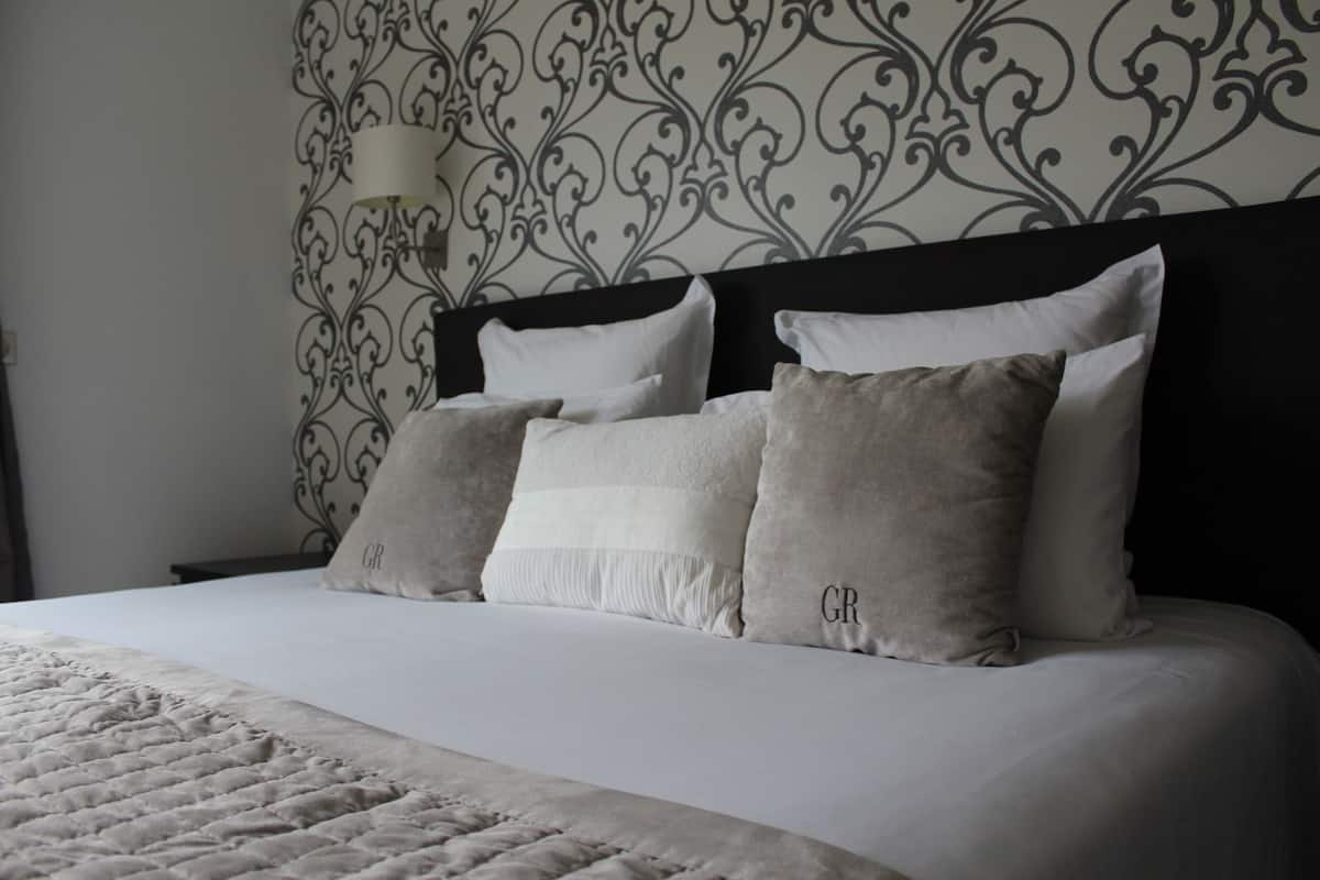 A neatly made bed with a quilted cover and several pillows, including a grey one with 'GR' embroidered on it.