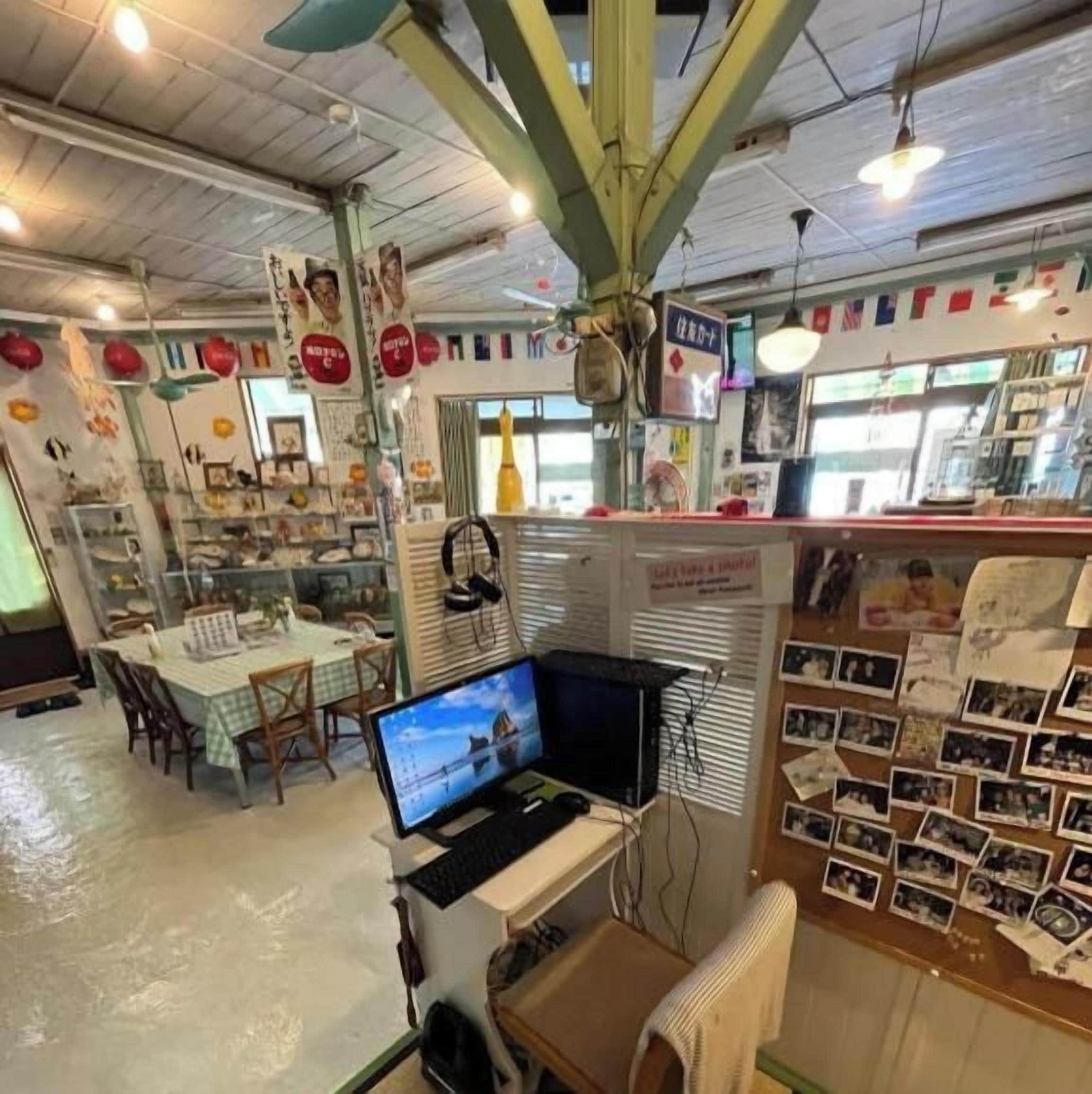 A room with a dining table, chairs, a computer, and a bulletin board with photos.