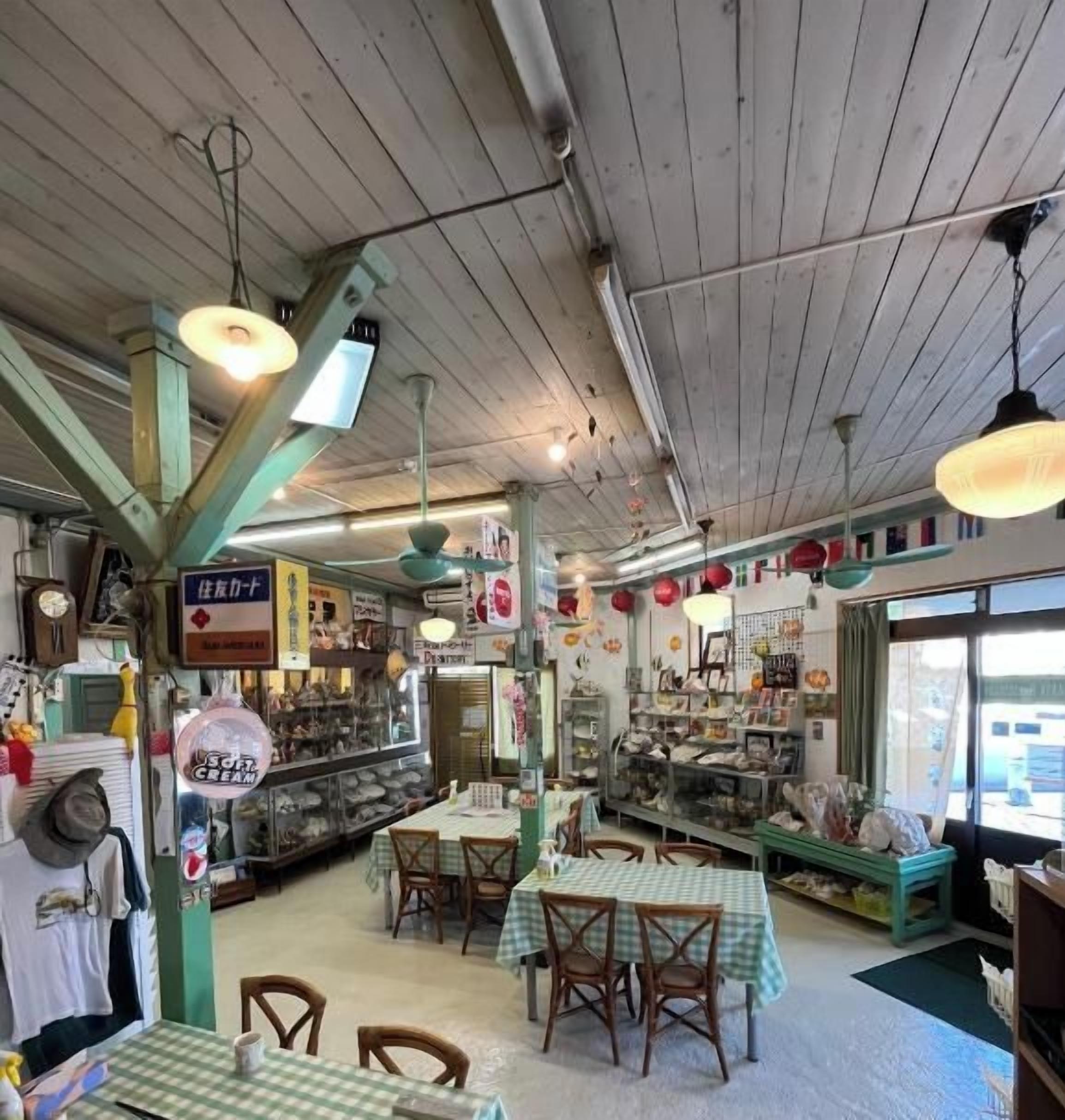 L’intérieur d’un restaurant avec des poutres en bois au plafond, des luminaires suspendus, des tables recouvertes de nappes à carreaux et divers plats présentés en arrière-plan.