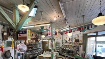 A restaurant interior with wooden ceiling beams, hanging lights, tables with checkered tablecloths, and various food items displayed in the background.