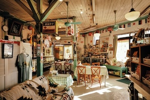 A cozy, well-lit room with wooden beams, checkered tablecloths, and various items on shelves and tables.