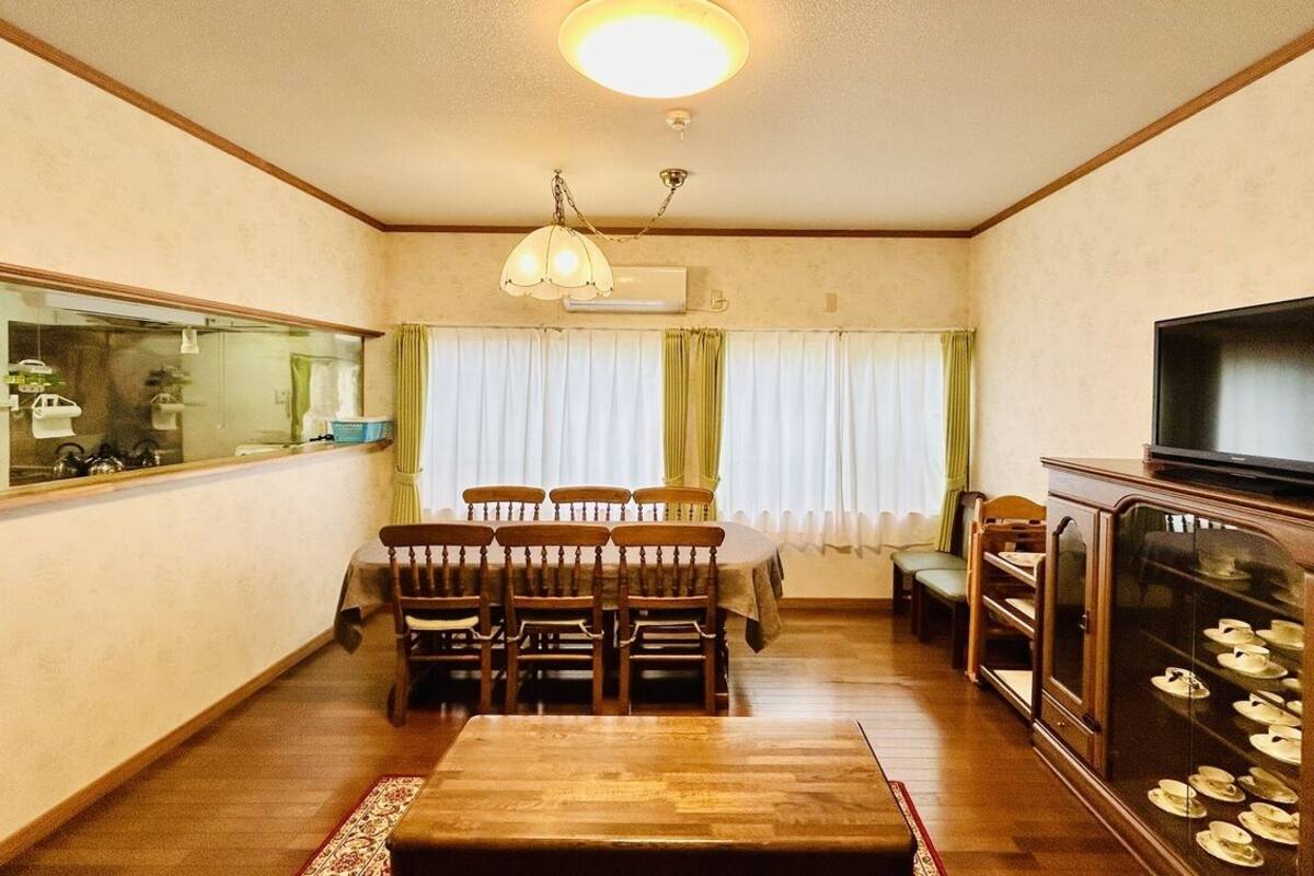 Uma sala de estar com uma mesa de jantar de madeira, cadeiras, uma televisão e um armário com sapatos.