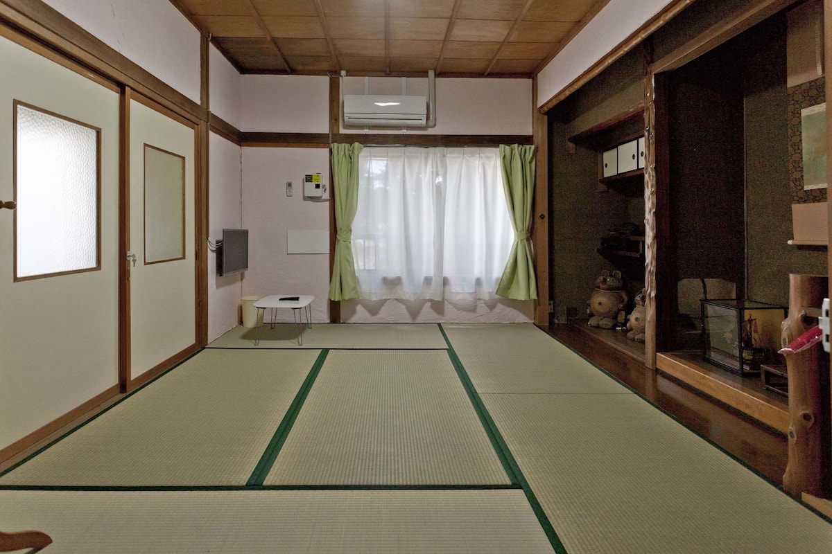Um quarto japonês tradicional com tatames, portas deslizantes, uma mesa pequena e uma estante com objetos decorativos.
