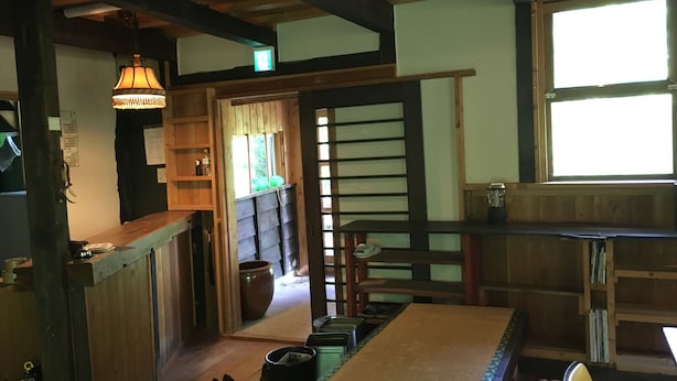 Una habitación tradicional japonesa con suelo de tatami, una mesa de madera baja, una lámpara colgante y una puerta corredera que da a otra habitación.