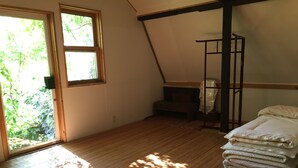 Una habitación con piso de madera, una cama con ropa blanca, un pequeño banco y una ventana con vista a la vegetación.