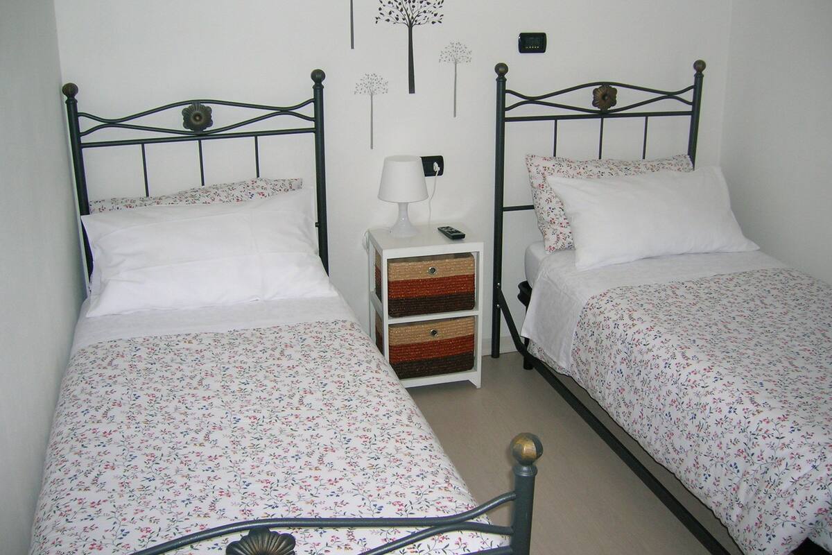 A twin room with two single beds, each with floral bedding, a bedside table with a lamp, and a wall clock.