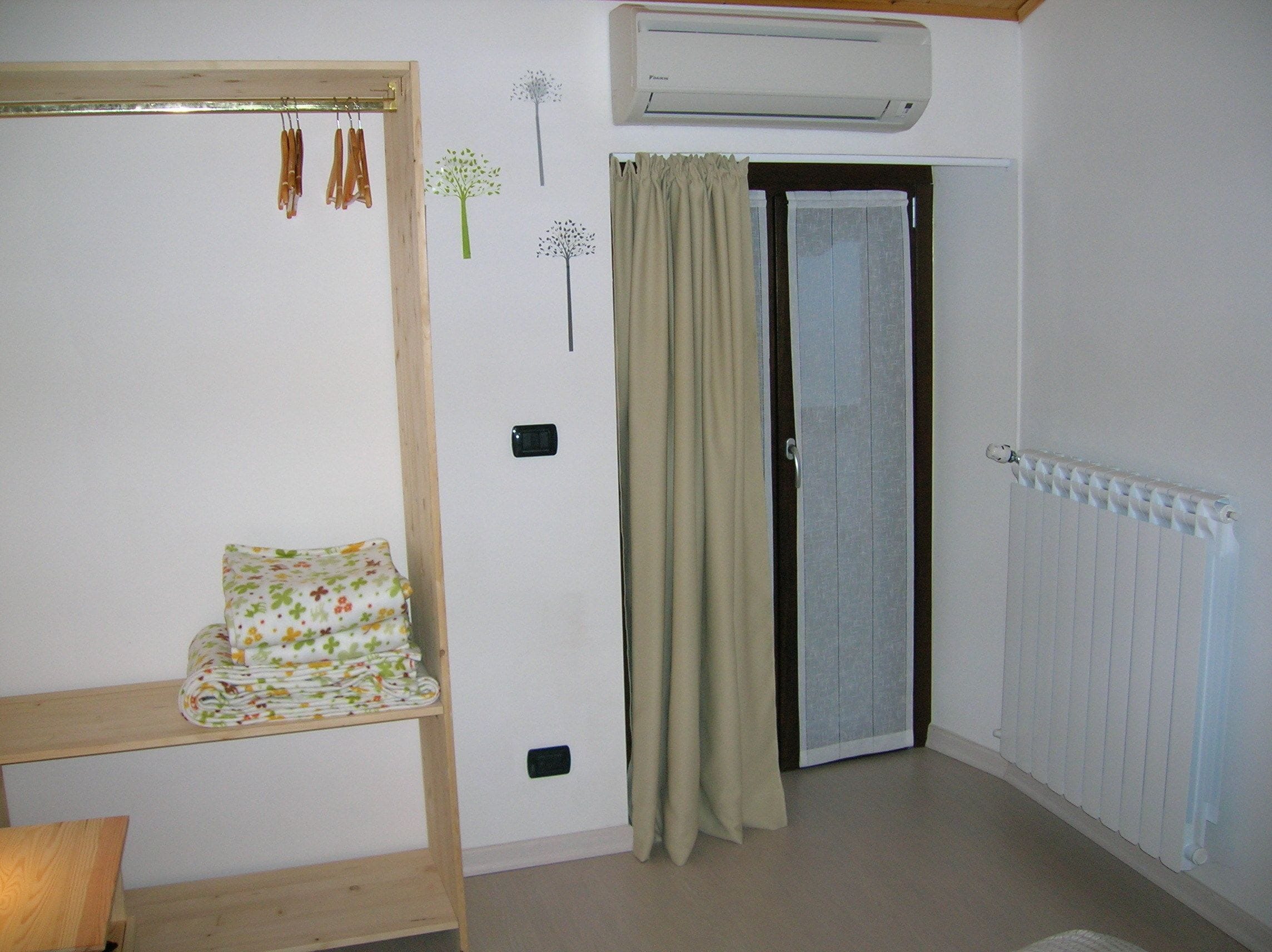 Une chambre avec un lit, un radiateur, un appareil de climatisation et une porte avec des rideaux.