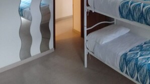 Una habitación con dos literas, un armario de madera y una puerta que da a otra habitación.