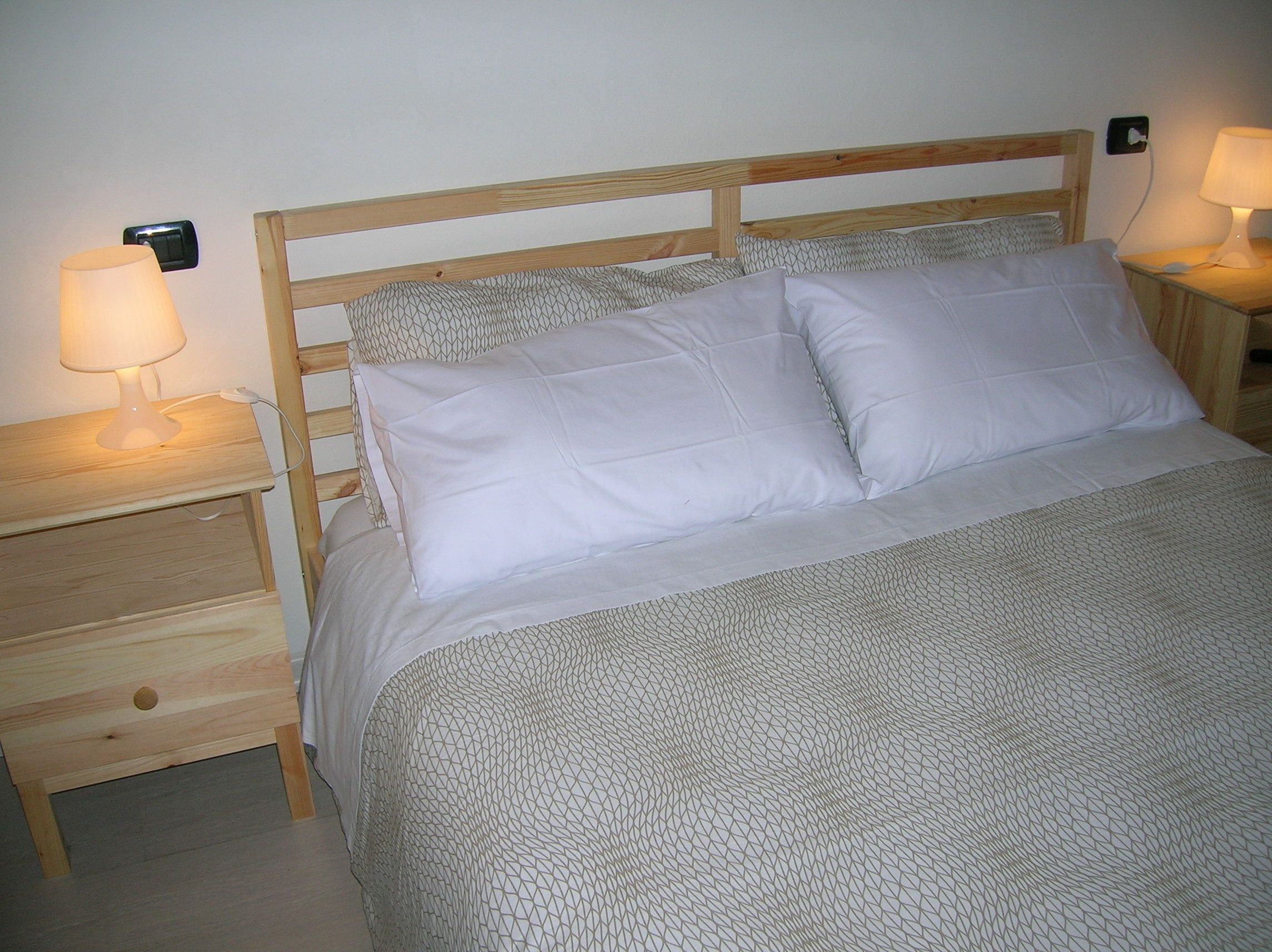 A neatly made bed with a geometric patterned bedspread, two bedside tables with lamps, and a wooden headboard.