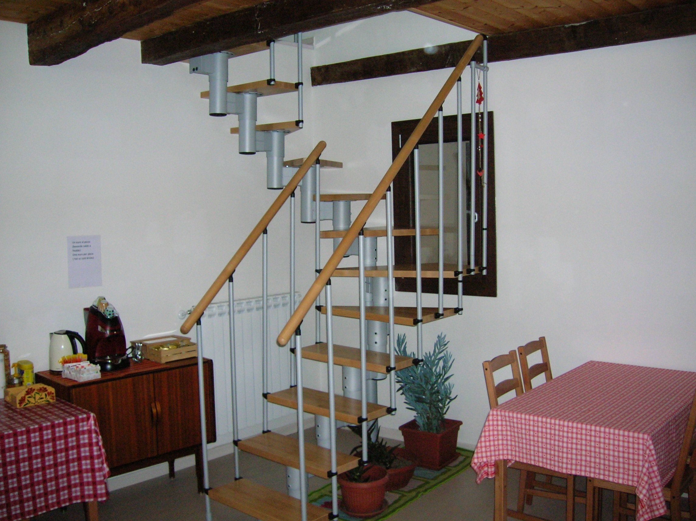 A staircase with a wooden handrail and metal balusters, a dining table with a checkered tablecloth, and a potted plant.