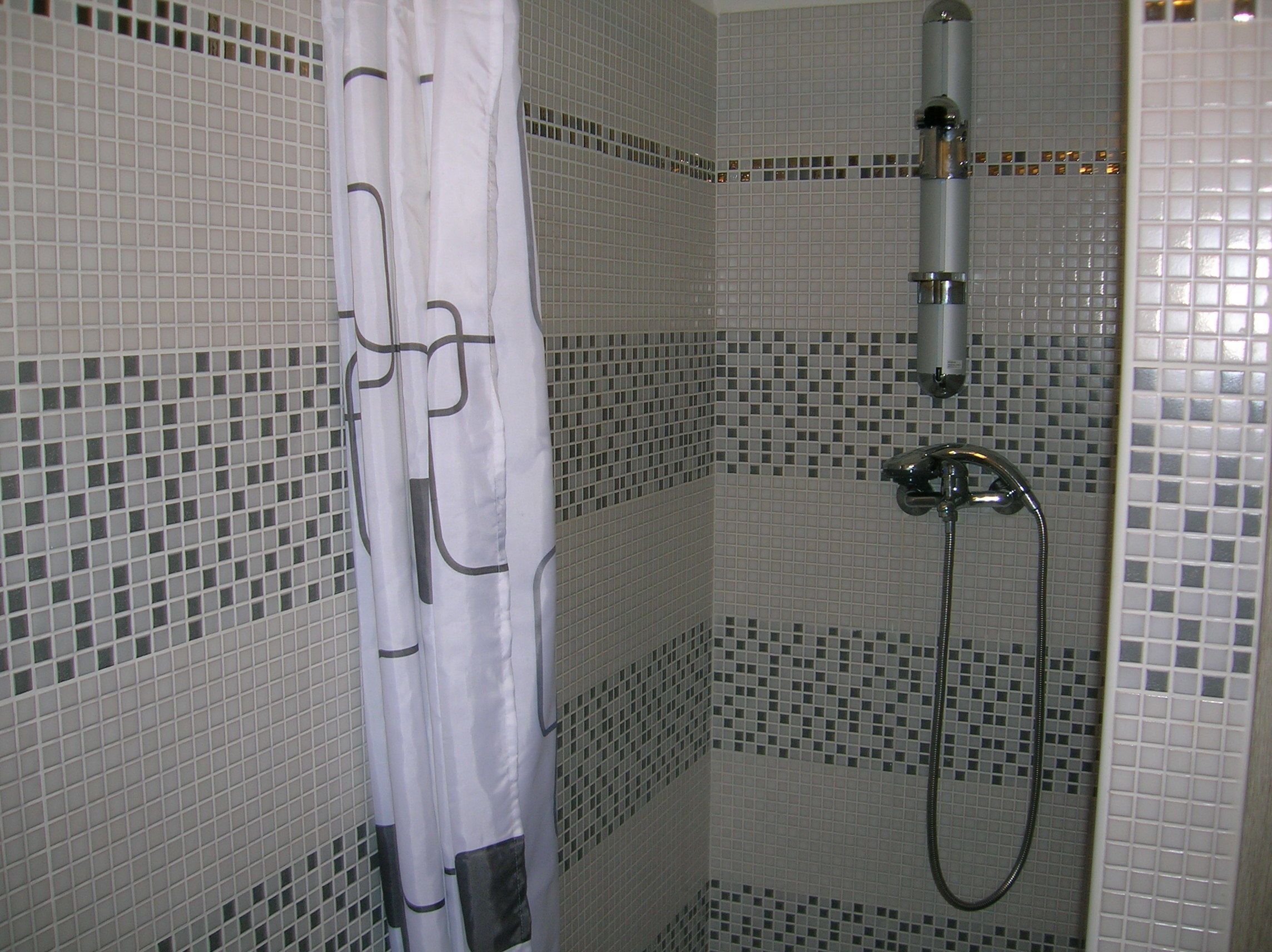 Ein Badezimmer mit Dusche, gefliesten Wänden und einer Duschvorhang.