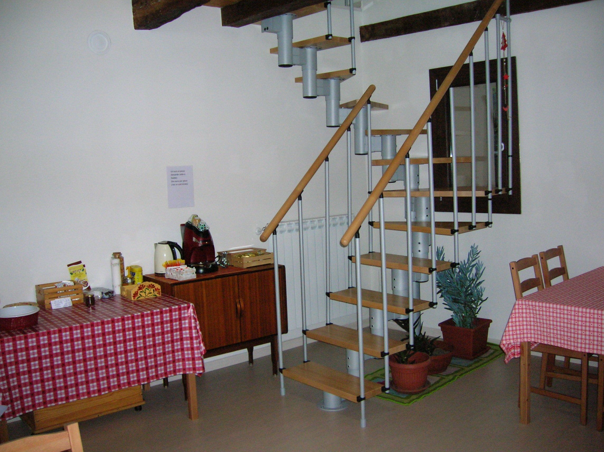 A dining area with a red and white checkered tablecloth, wooden chairs, a staircase with metal railings, and potted plants.