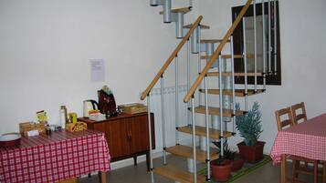 A dining area with a red and white checkered tablecloth, wooden chairs, a staircase with metal railings, and potted plants.