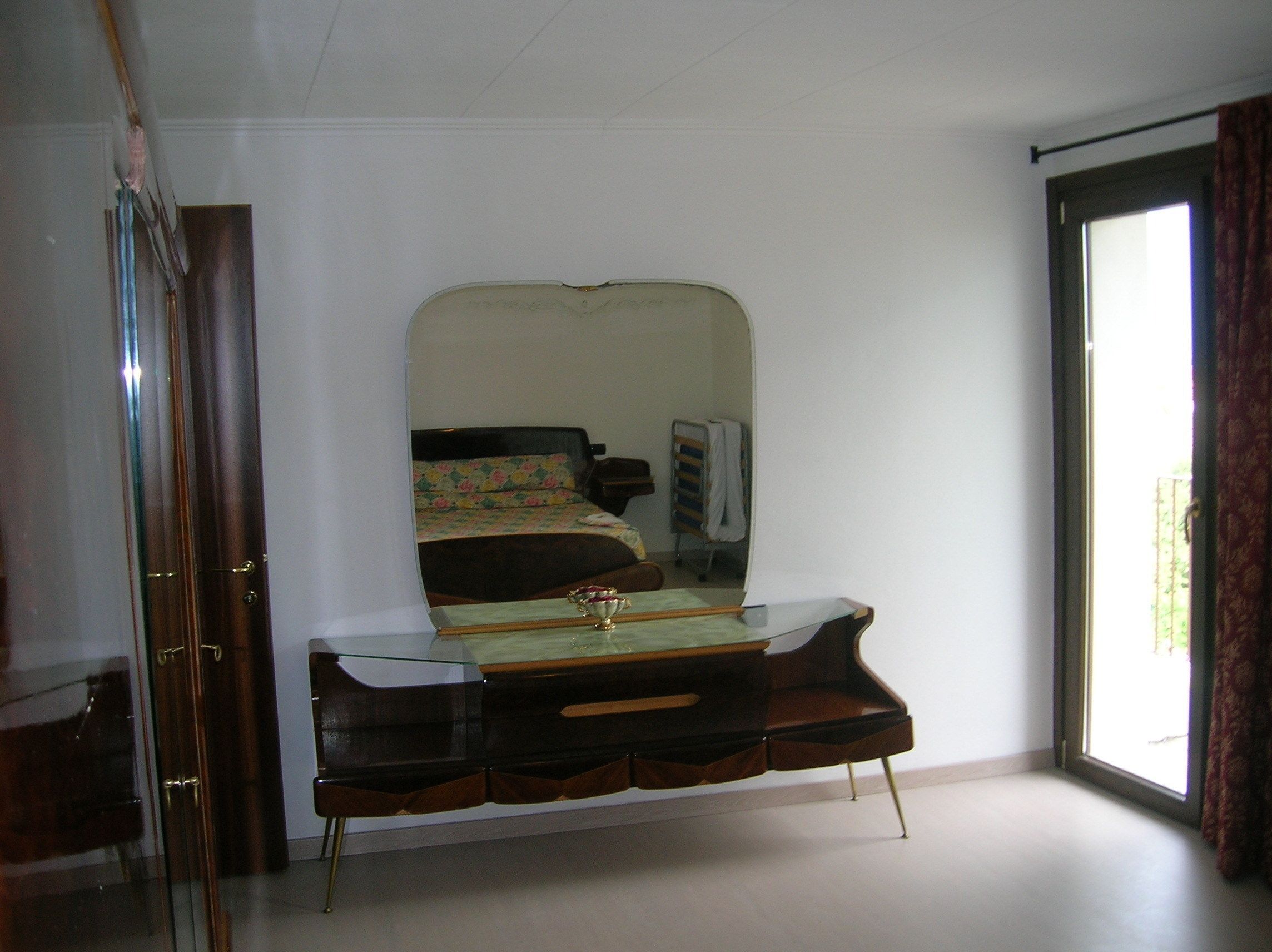A bedroom with a large mirror, a bed with floral bedding, a dresser, and a window with curtains.