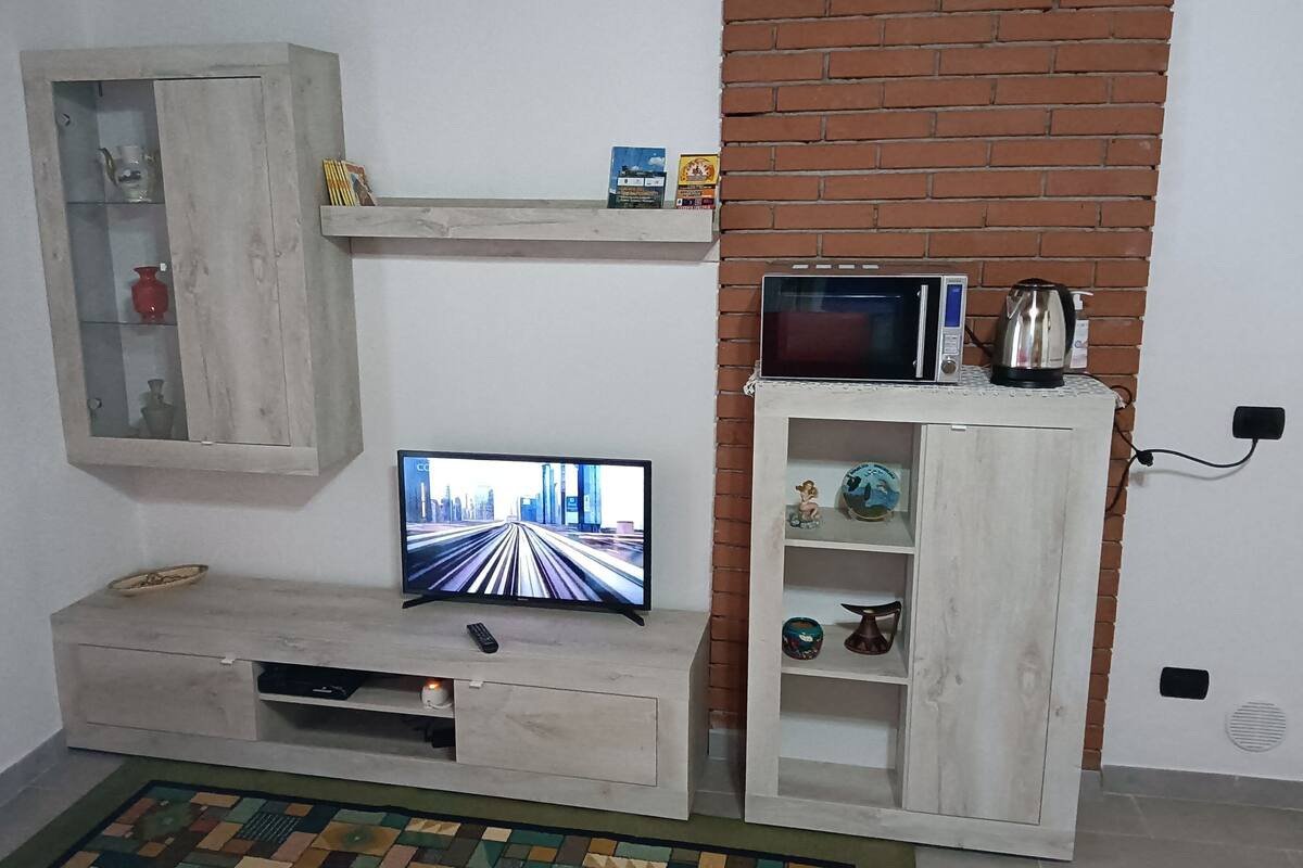 A living room with a television, a coffee machine, and a shelf with decorative items.