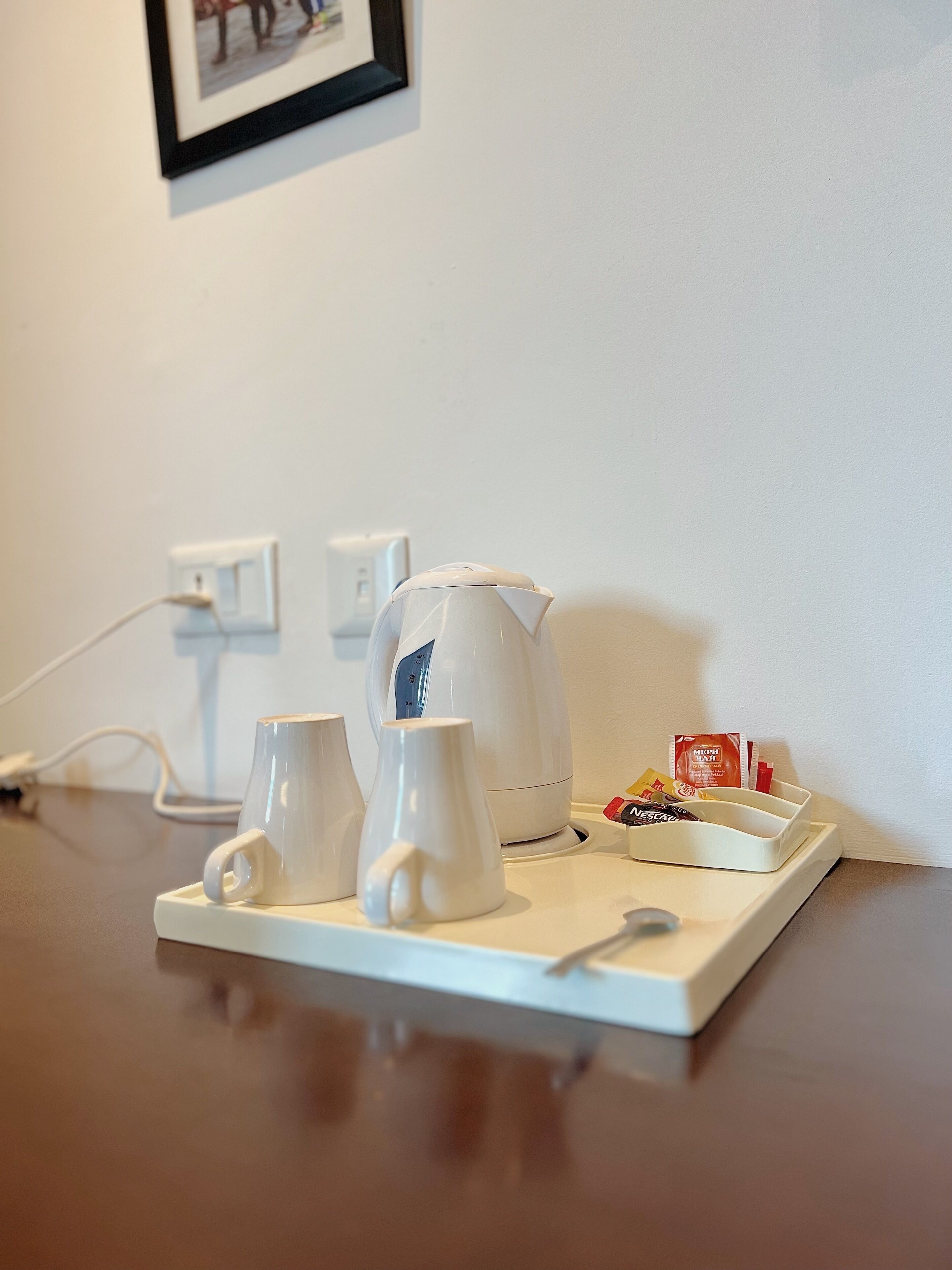A coffee station with a kettle, cups, and a tray with coffee pods.