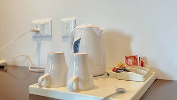 A coffee station with a kettle, cups, and a tray with coffee pods.