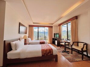 A hotel room with two beds, a desk with a chair, a TV, and a view of mountains.