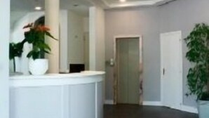 A modern reception area with a curved white counter, dark tiled flooring, and potted plants. - Alba Hotel (Ravenna)