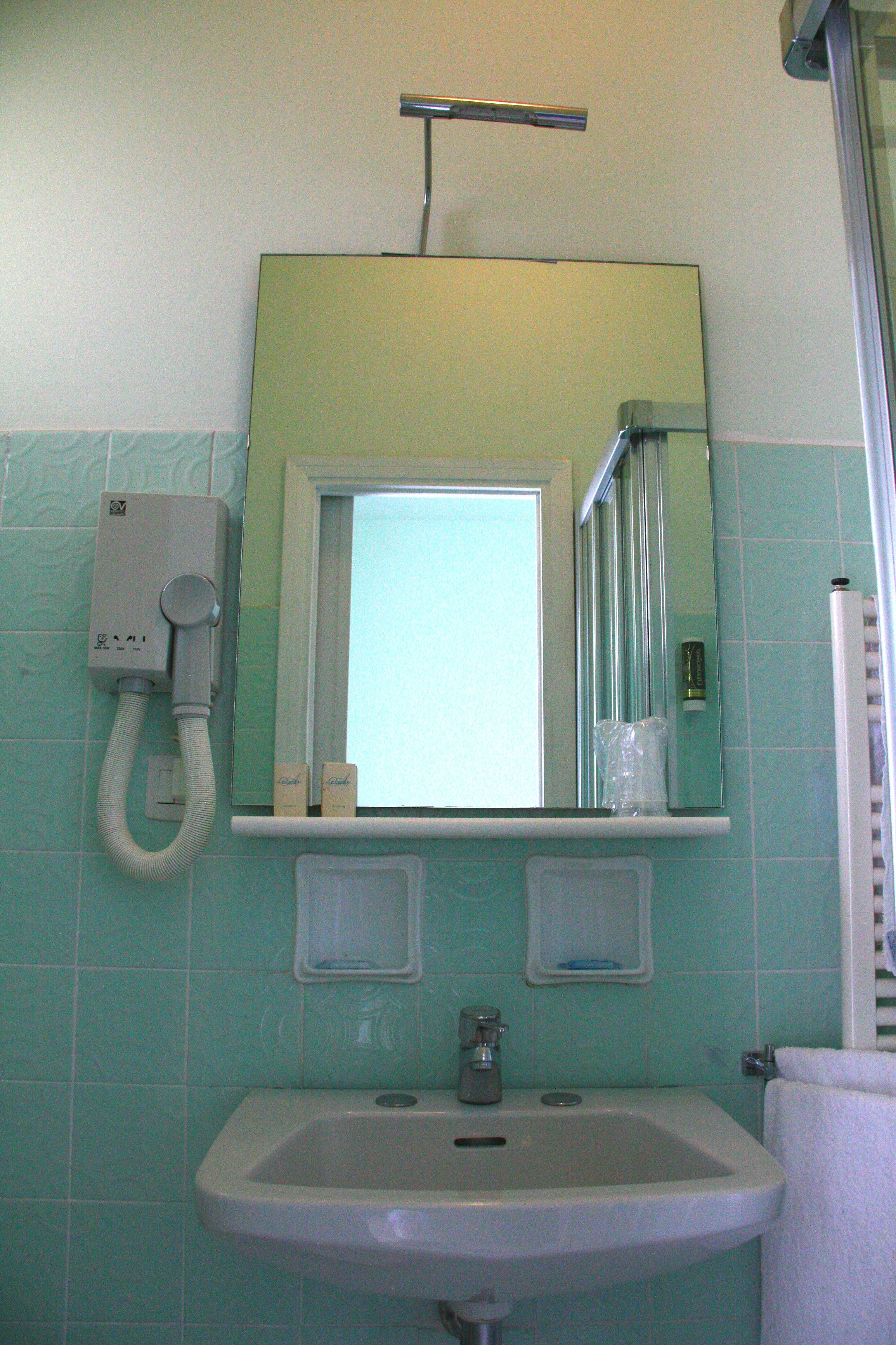 Een badkamer met een wastafel, spiegel, handdoekhouder en douche.