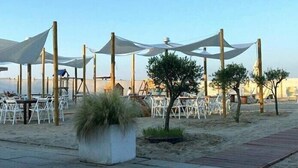 An outdoor seating area with white chairs and tables, shaded by white canopies, and a small planter with grass. - Alba Hotel (Ravenna)