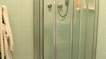 A glass-enclosed shower stall with a handheld showerhead, a white toilet, and a towel rack with towels.