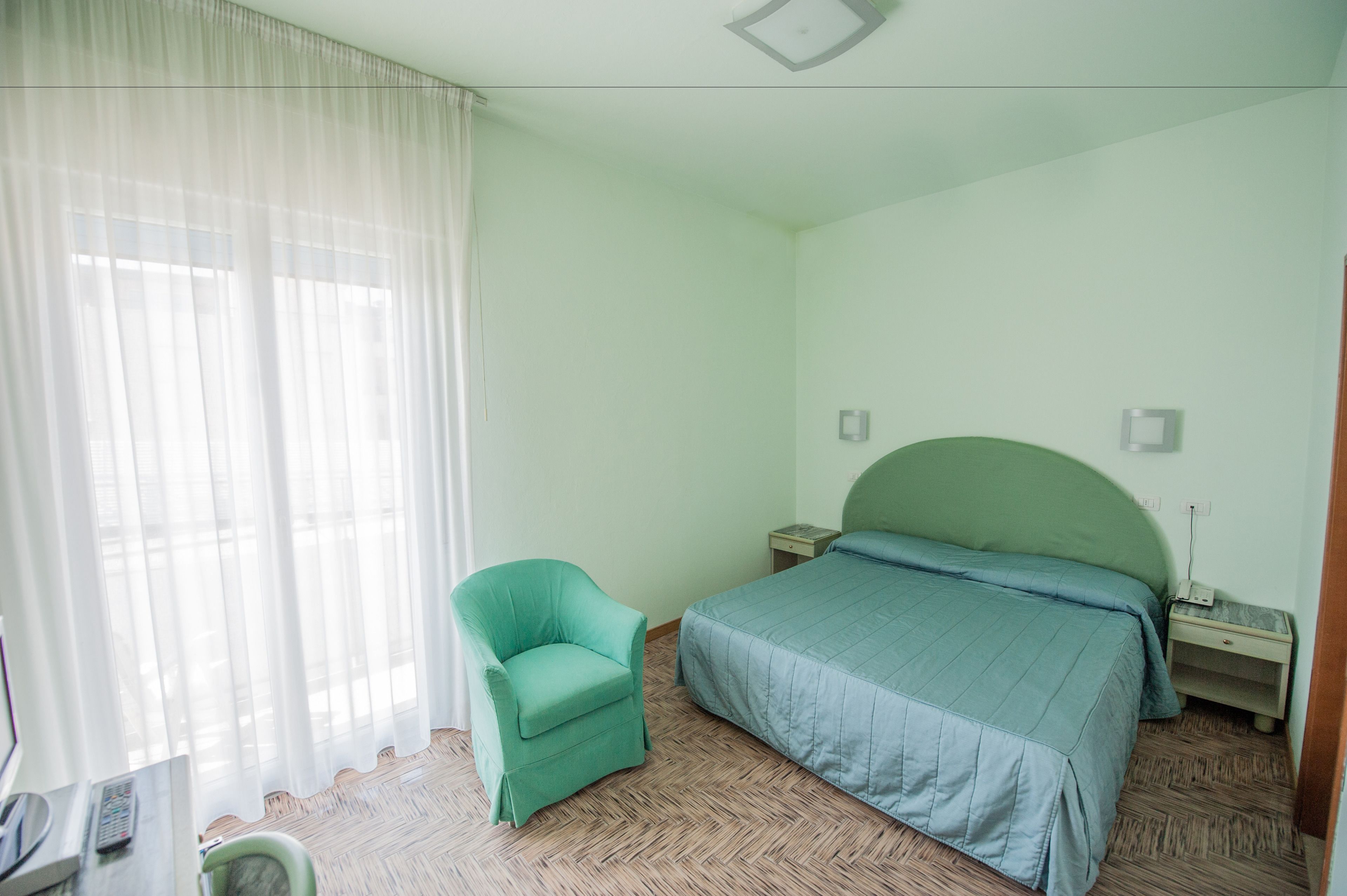 Une chambre à coucher avec un lit, une chaise, une table de chevet et une fenêtre avec des rideaux.