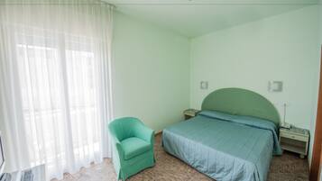 Une chambre à coucher avec un lit, une chaise, une table de chevet et une fenêtre avec des rideaux.