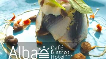 Un plat de poisson servi dans une assiette bleue, agrémenté de quelques garnitures, présenté au Café Bistro Hotel à Marina di Ravenna.