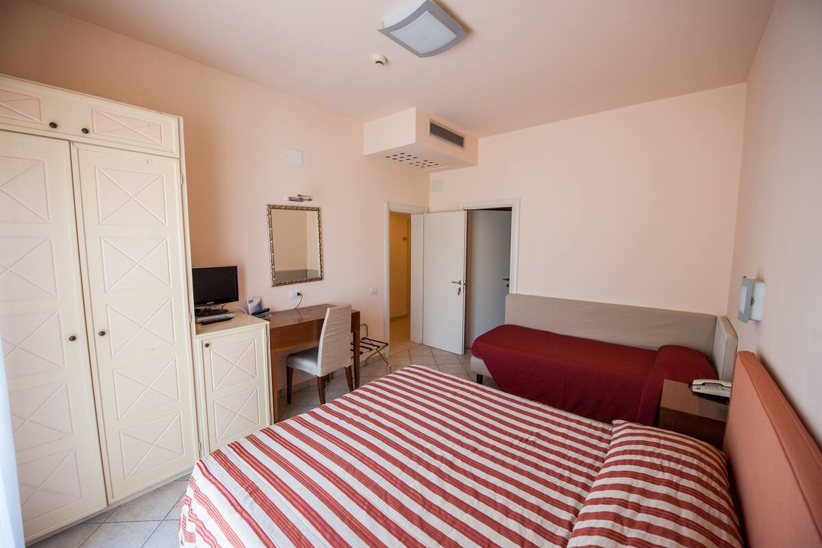 Un dormitorio con cama, escritorio, silla, armario y puerta que da a otra habitación.