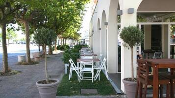 An outdoor seating area with white chairs and tables, a potted tree, and a building with a sign reading "FINISTERRE CAFÉ".