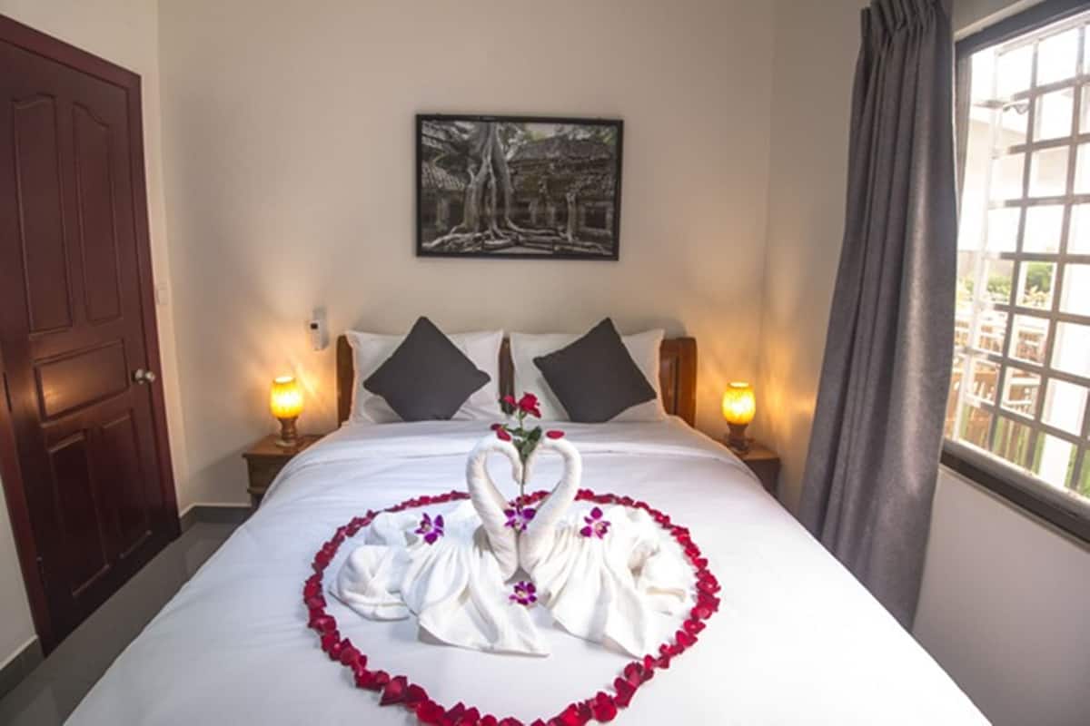 A hotel room with a bed, pillows, a painting on the wall, and a window with curtains.