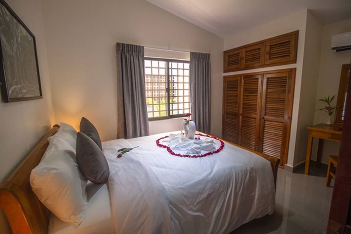 A hotel room with a bed, a window with curtains, a wooden wardrobe, and a framed picture on the wall.