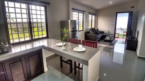 A modern kitchen with a central island, dining area with chairs, and a living room with a sofa and coffee table. - Ry's Lotus Resort d'Angkor (Siem Reap)