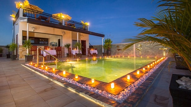 A poolside area with a pool, a building with a balcony, and a row of candles along the pool's edge. - Ry's Lotus Resort d'Angkor (Siem Reap)