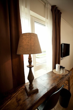 Un bureau en bois, une lampe, une chaise et un téléviseur fixé au mur.