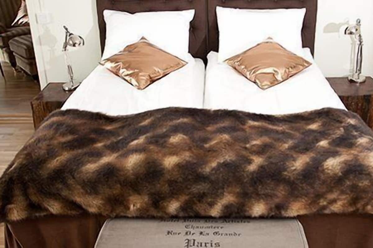 Una cama con una manta de piel sintética, dos almohadas y una mesita de noche con una lámpara.