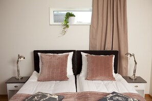 Un lit double avec deux oreillers, une table de chevet avec une lampe, une fenêtre avec une plante et un rideau.