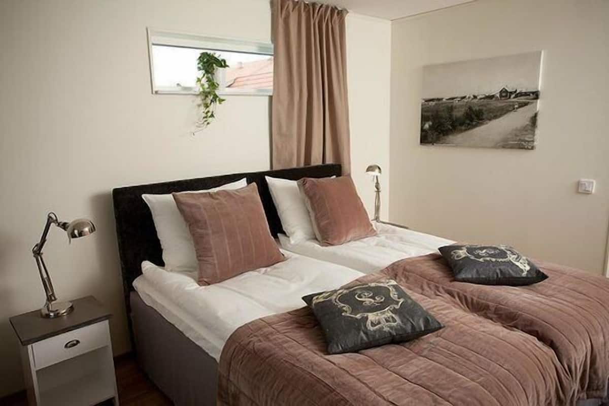 Un dormitorio con cama, lámpara de noche y ventana con cortinas.